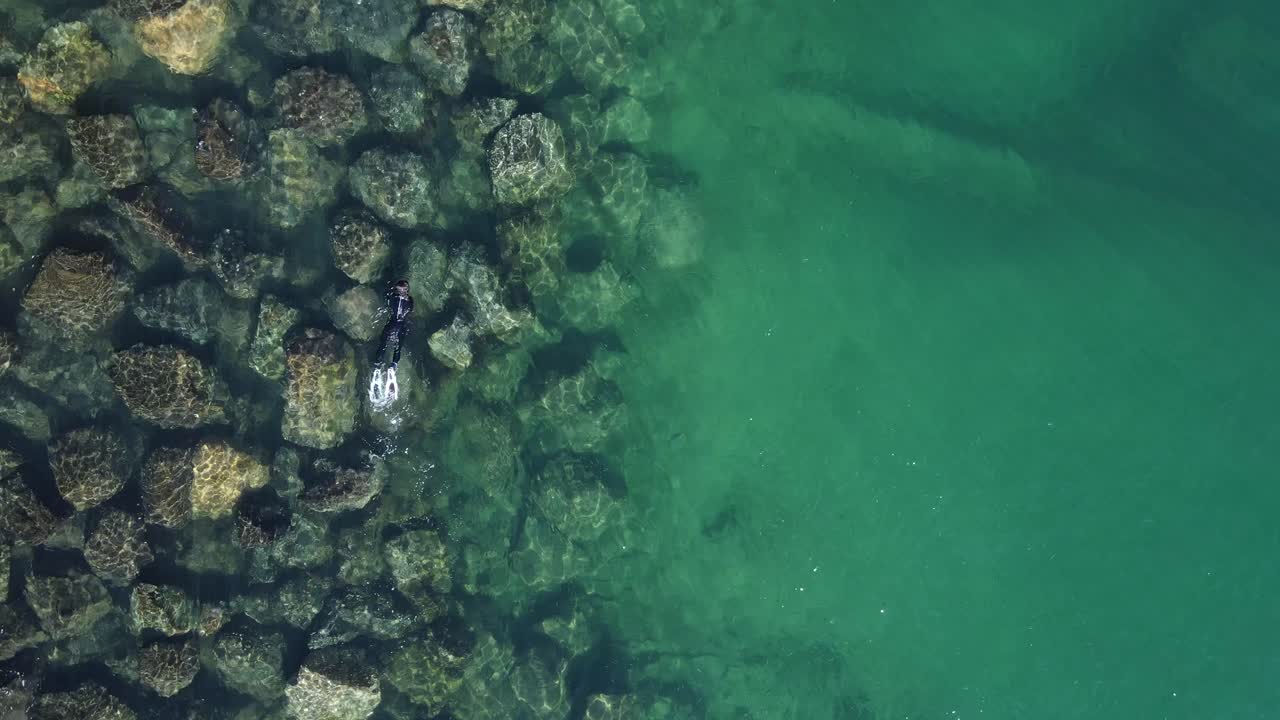 Una persona che fa snorkeling sopra grandi massi posizionati sott'acqua per creare una barriera corallina artificiale.