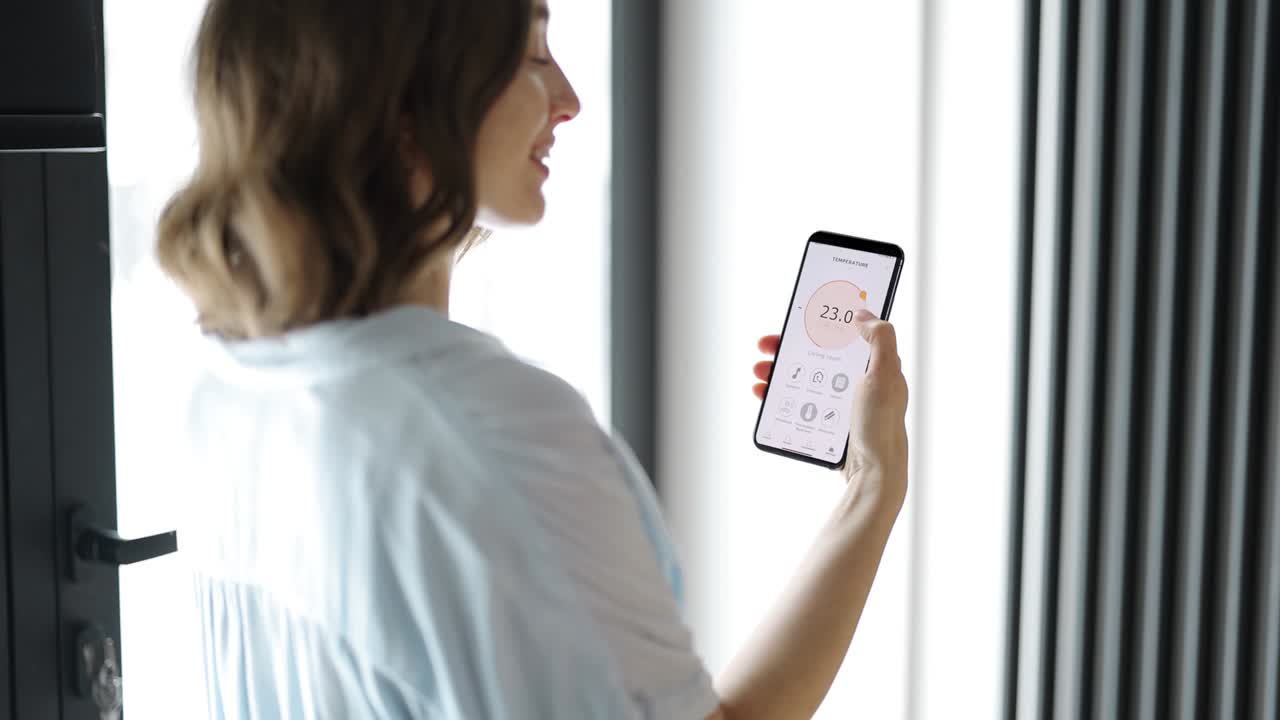 mujer ajustando la temperatura de la habitación con un teléfono inteligente