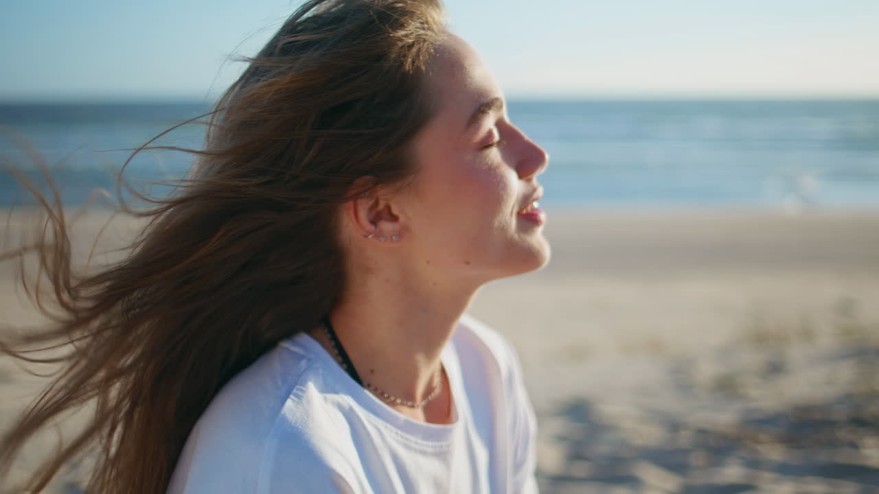 Donna in estate che beve acqua e si gode la spiaggia con vista sull'oceano. Ritratto di una donna con i capelli al vento