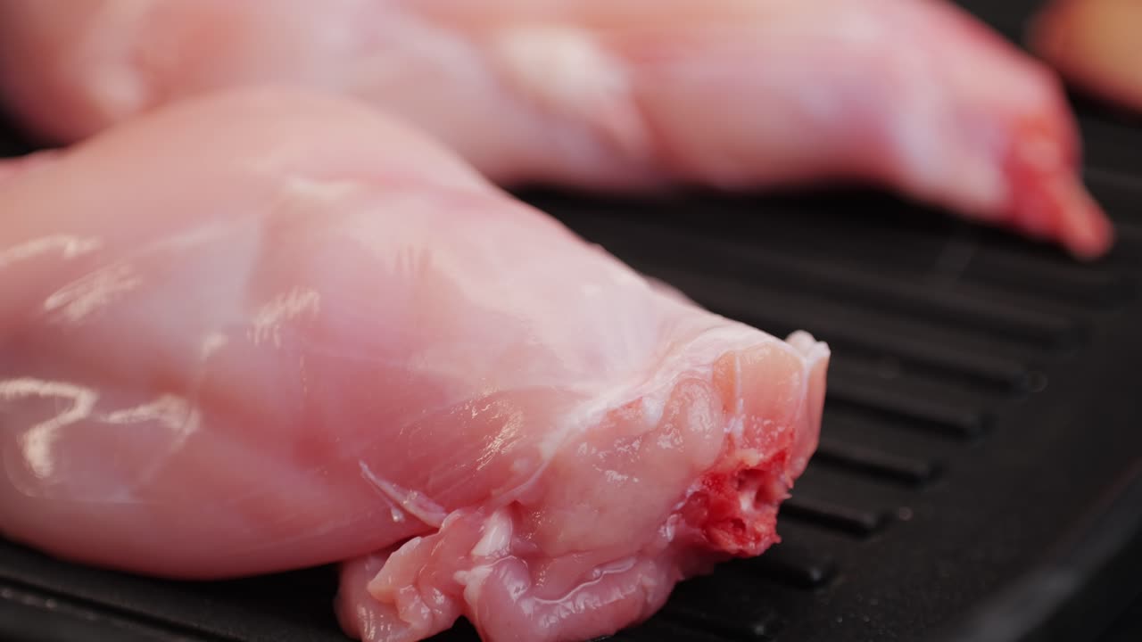 Cosce di coniglio arrosto in una padella grill, primo piano di carne salutare per la dieta, chef che cucina coniglio nella cucina del ristorante, sfondo nero. Vista dall'alto