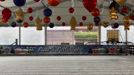 little girl skating alone on ice alone in indoor ice rink with christmas decorations hanging on ceiling