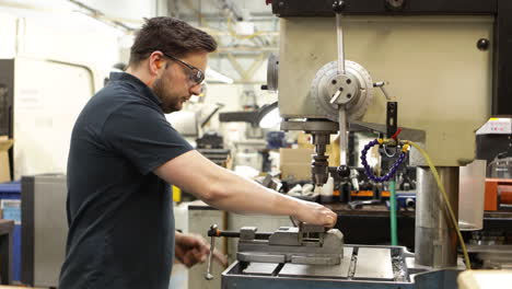 worker clamping metal block, drilling in drill press