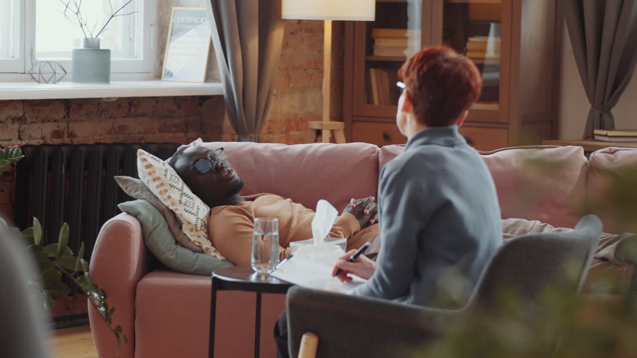 소파에 누워 있는 흑인 남자가 심리학자와 대화하고 있습니다.