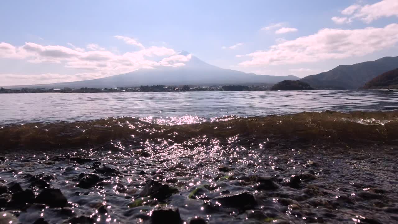 후지산이 있는 자갈 해변에 부서지는 작은 파도의 낮은 각도