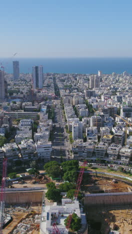 vertical video pull back reveal the kikar (square ) hamedina impressive project construction - tel aviv beaches in the background