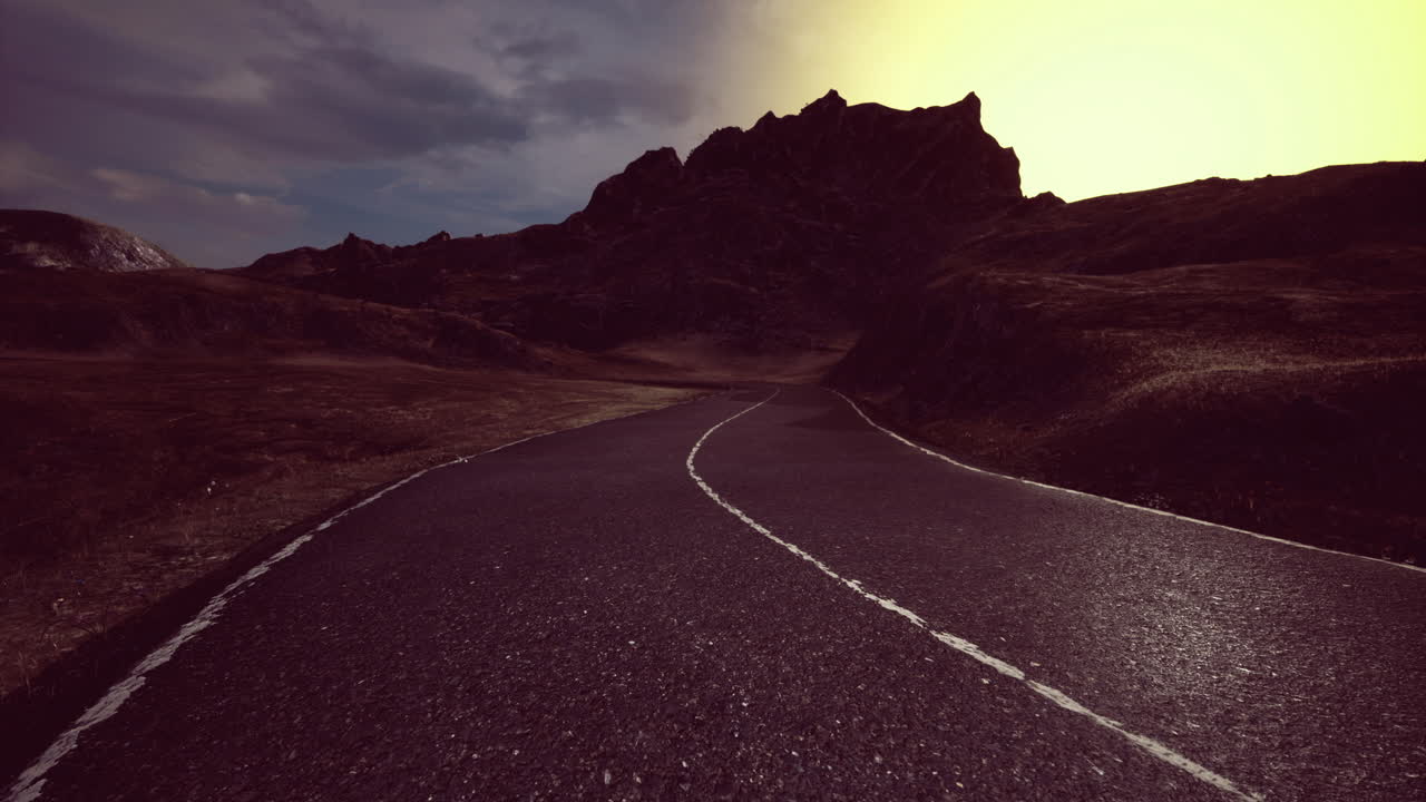 Winding road leading toward majestic mountains at dawn with vibrant colors