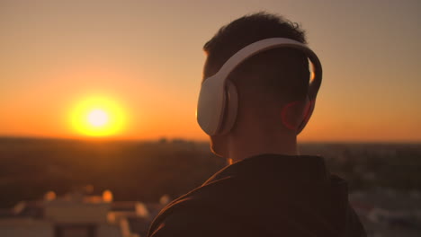 close-up of a man in headphones looking at the city from the height of a skyscraper at sunset. relax while listening to music. enjoy a beautiful view of the city at sunset from the roof with headphones.