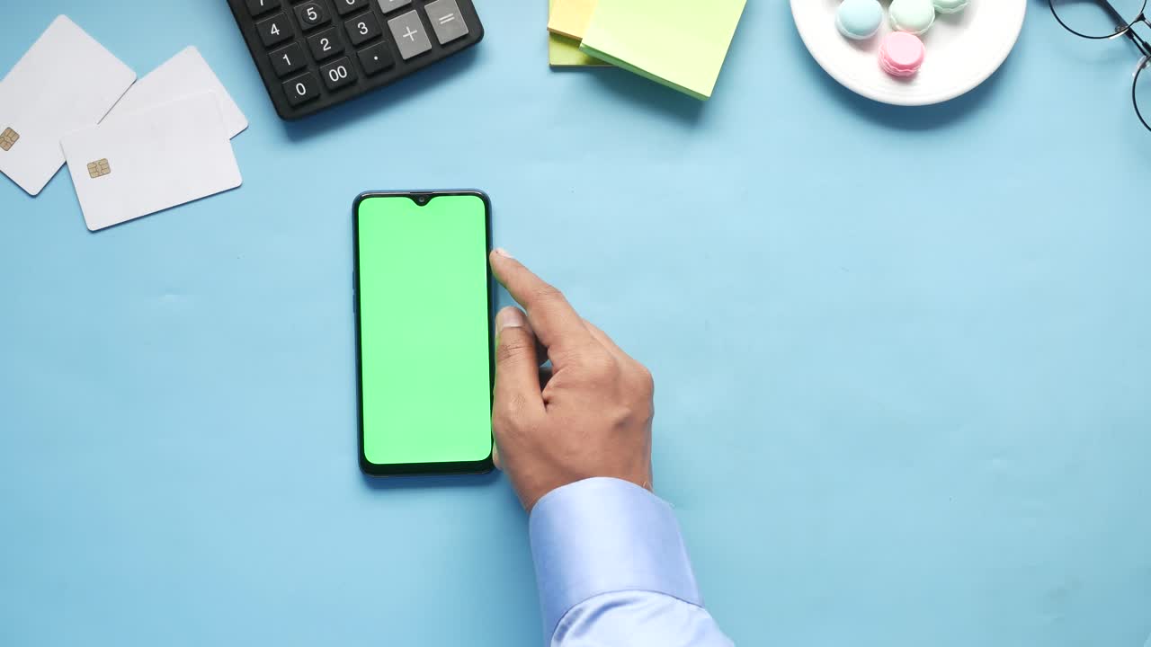 Person using a smartphone with green screen on a desk