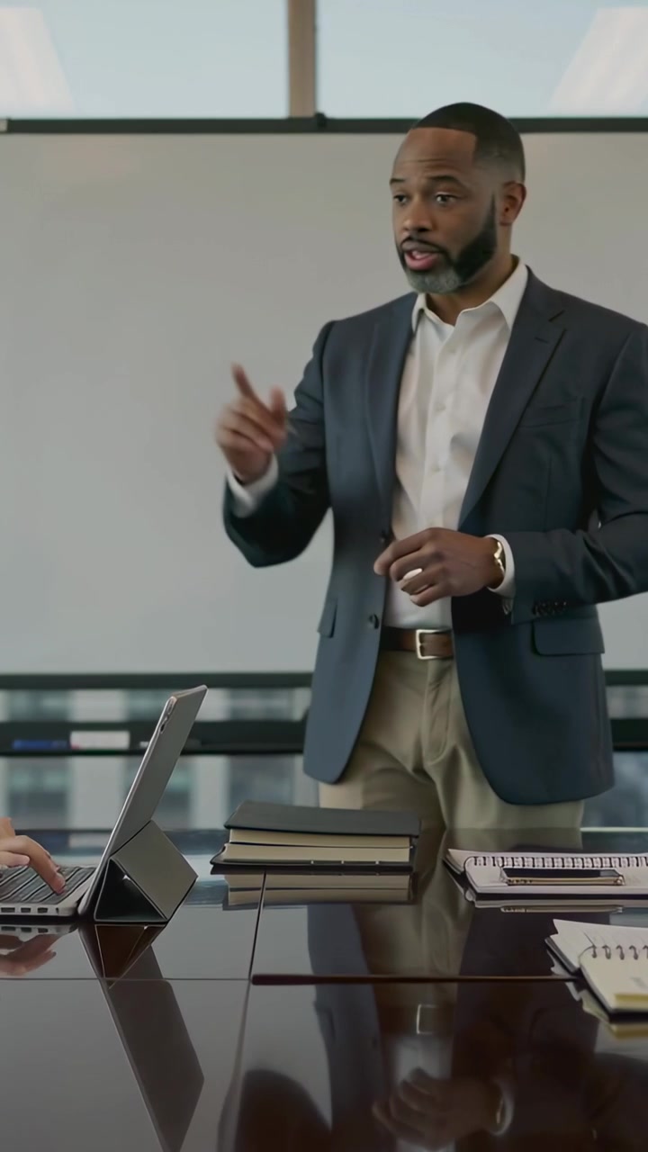 Vertical video: Pointing to whiteboard, presenter in blazer presenting to team at table with laptop