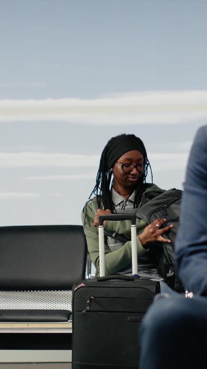 Video verticale: Donna in aeroporto con l'essenziale per il viaggio, seduta su una panchina mentre aspetta.
