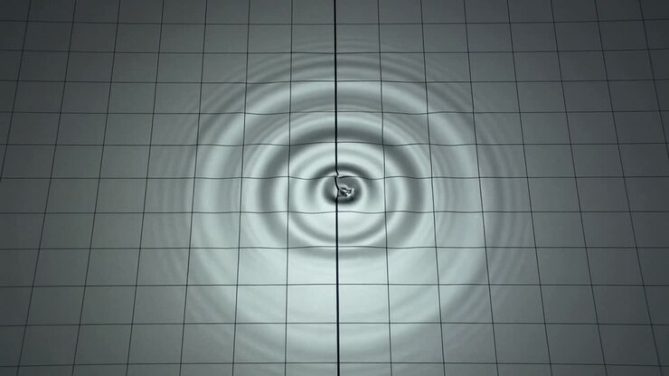 Vertical video: Descending rod creating concentric ripples on gridded plane, for measurement