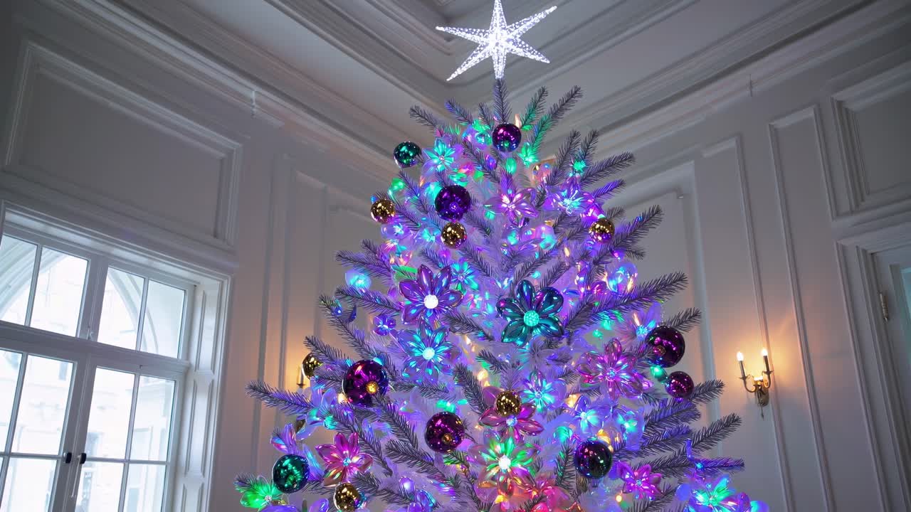 Festive white Christmas tree adorned with colorful lights, delicate flower ornaments, and gleaming ball decorations, softly changing colors within elegant classic white interior
