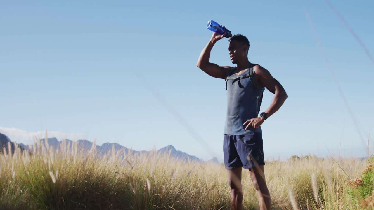 hombre afroamericano haciendo ejercicio al aire libre bebiendo agua en el campo en una costa