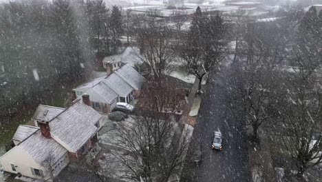 Car-driving-towards-drone-during-snow-storm-in-American-neighborhood