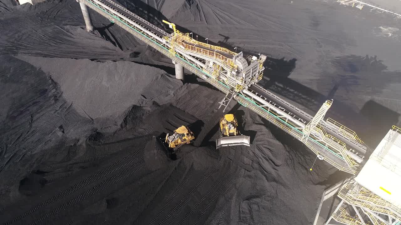 Drone shot of Coal Mine Plant, Coal coming off conveyor belt with caterpillar mining trucks moving the coal around