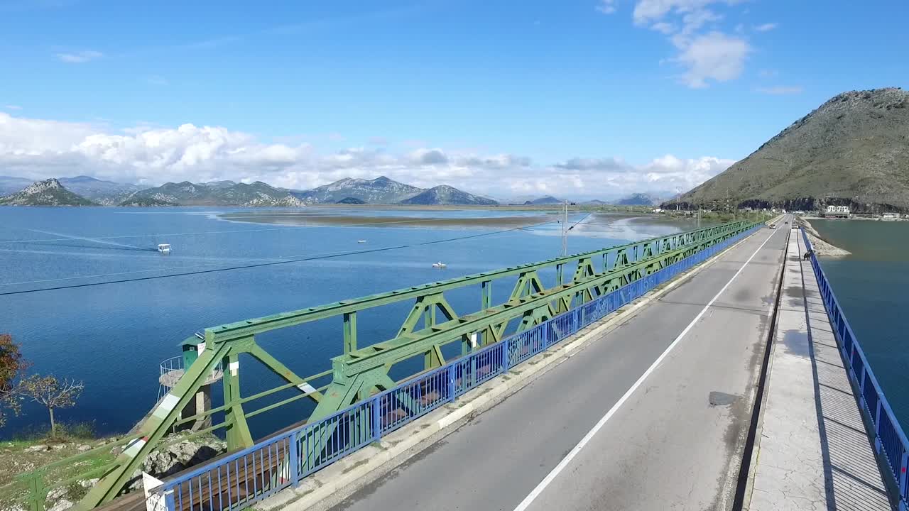 배경 에 산 들 이 있는 호수 를 가로지르는 다리 에 있는 컨버터블 자동차