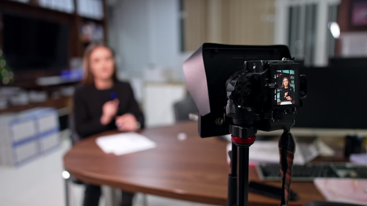 Woman sitting in the office creating content for her blog. Professional camera records female speech. Blurred backdrop.
