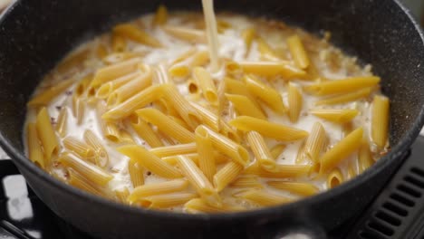 cocinero anónimo añadiendo crema a la sartén con macarrones