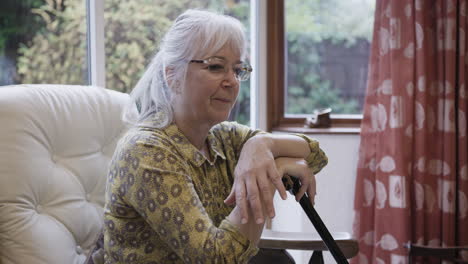 older woman sitting indoors with a cane