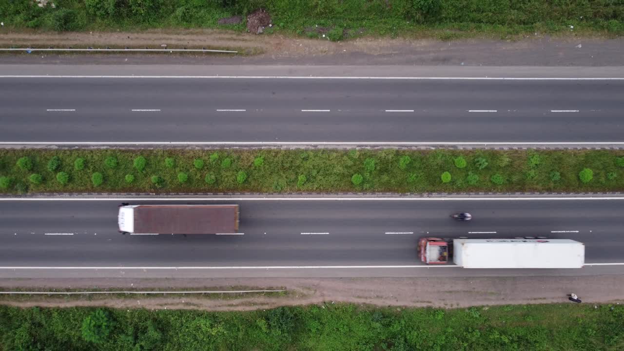 Top-down aerial view of a four-lane highway in India with pedestrians, motorcycles, passenger cars and freight trucks passing