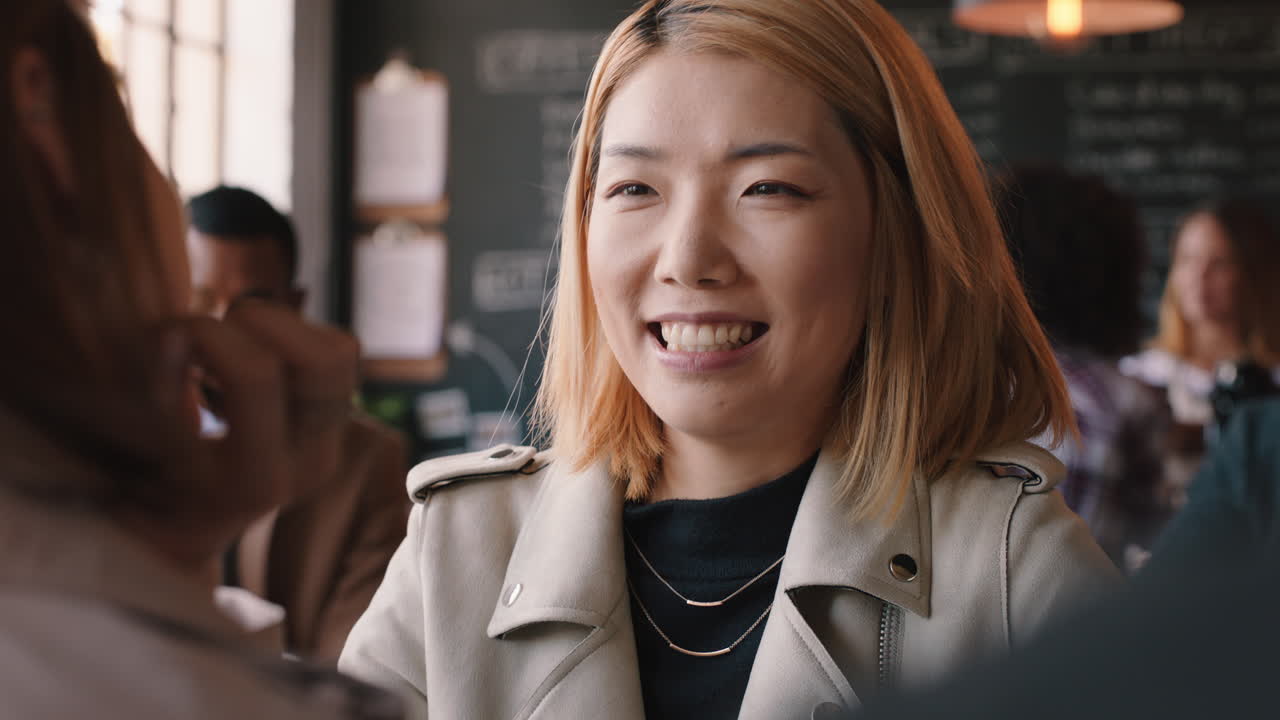 아름다운 아시아 여성이 카페에서 친구와 채팅하고 사교를 즐기고 바쁜 레스토랑에서 대화를 나누고 있습니다.