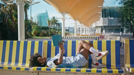 teen reader enjoy literature lying on campus bench sunny day. girl reading book