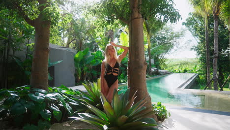 beautiful blonde woman in black swimsuit relaxing by the pool in tropical paradise