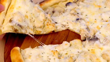 man takes a slice of pizza with mushrooms champignons and cheese on wooden board on the table.