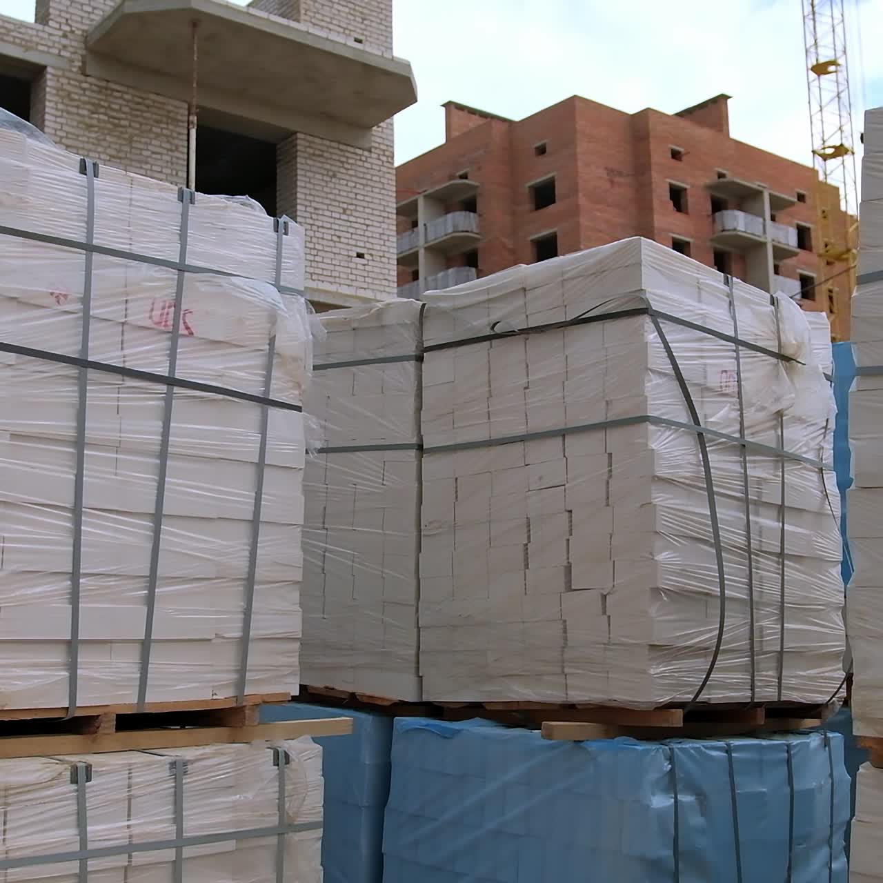 White brick piles covered with plastic. Construction site outdoors. Unfinished blocks of flats at backdrop