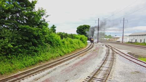 Una-Vista-Elevada-De-Un-Gran-Tren-De-Pasajeros-Con-Motor-De-Vapor-Que-Sopla-Humo-Pasando-Por-Un-Apartadero-En-Un-Día-Nublado