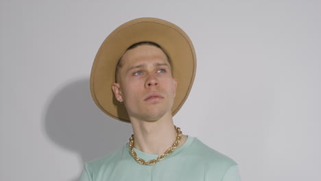 young model posing with big brown hat, golden necklace and green t shirt