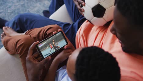 composite of father and son at home watching athletics running event on smartphone