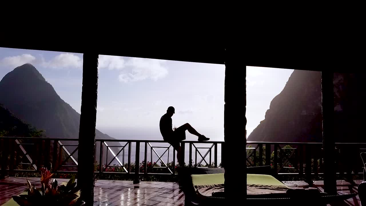 한 남자가 세인트 루시아 캐리비안의 고급 호텔 객실 발코니에 앉아 있습니다.