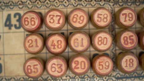 Filmische-Nahaufnahme-Eines-Bingo-Holzfässers,-Holzige-Figuren,-Auf-Einem-Strukturierten-Hintergrund-Mit-Alten-Zahlen,-Vintage-Brettspiel,-Professionelle-Beleuchtung,-Zeitlupe-120-Fps