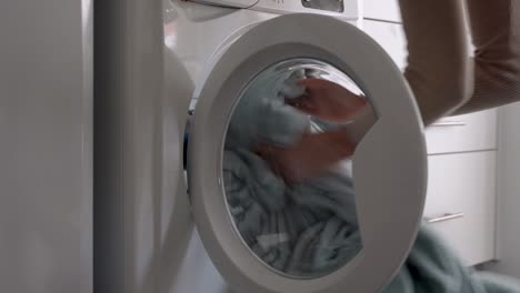 female put blanket into laundry machine, load clothes to washer machine and close door