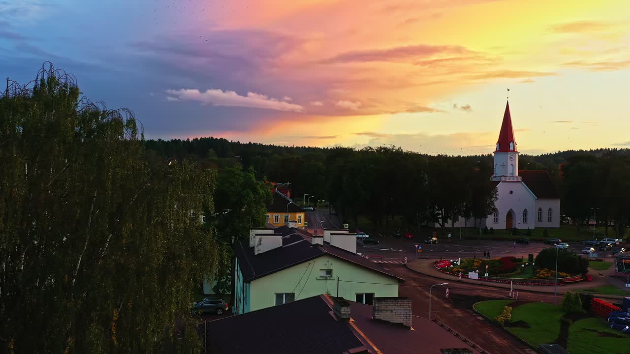 Latvian town Smiltene with church tower under purple-orange sky at sunset with bird flock