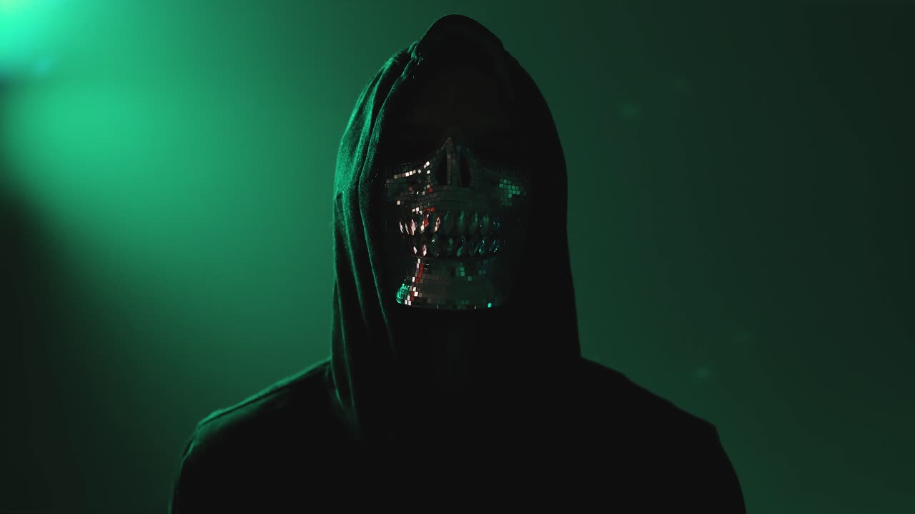 Masked Hacker Standing with Arms Crossed Facing Camera in Darkness – Concept of Cybersecurity Threat, Blackmarket Activity and Digital Intrusion
