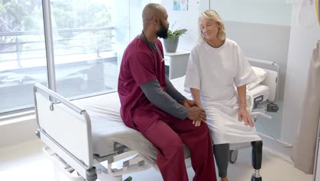 african american male doctor talking to caucasian female patient with prosthetic leg at hospital