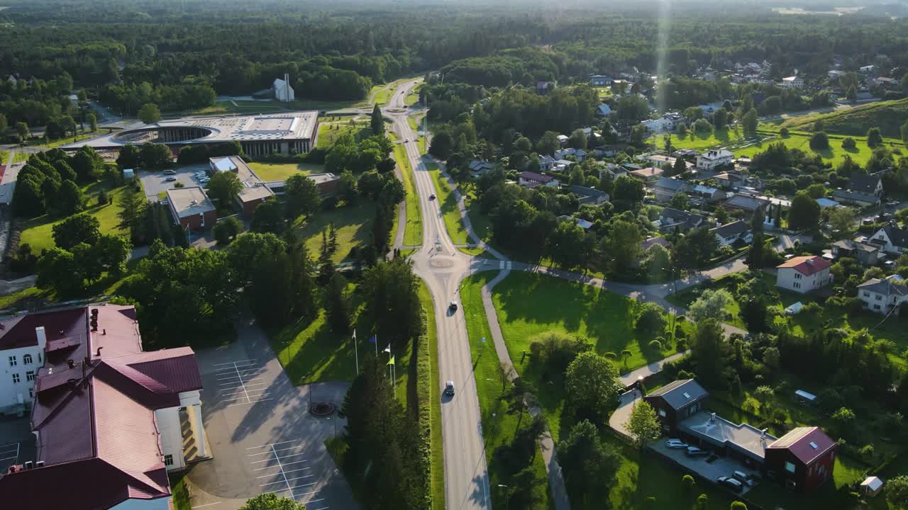 Aerial drone hyperlapse of a small town or a city with traffic moving fast in front of a historic old white majestic library during summer sunset. Chimney smoking in the horizon and forest is visible