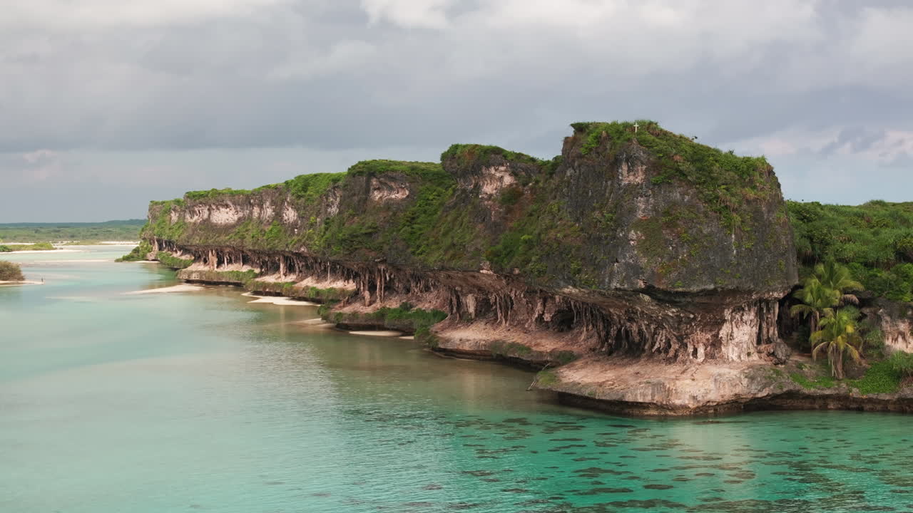 Drone footage of Lekini Bay, Ouvéa, showing turquoise lagoon waters, dramatic cliffs, coral reef patches and lush green tropical vegetation along the coast