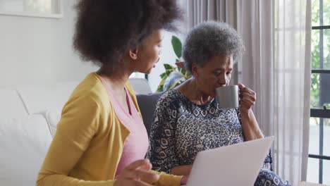 happy african american adult daughter and senior mother using laptop at home, slow motion