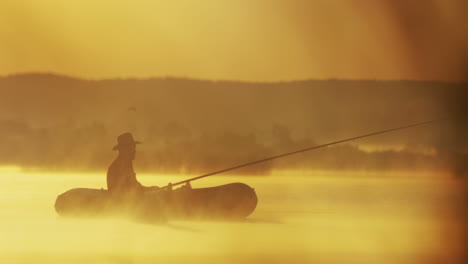 fernsicht auf einen alten mann mit hut auf einem boot, der an einem bewölkten morgen mit einer rute auf dem see fischt