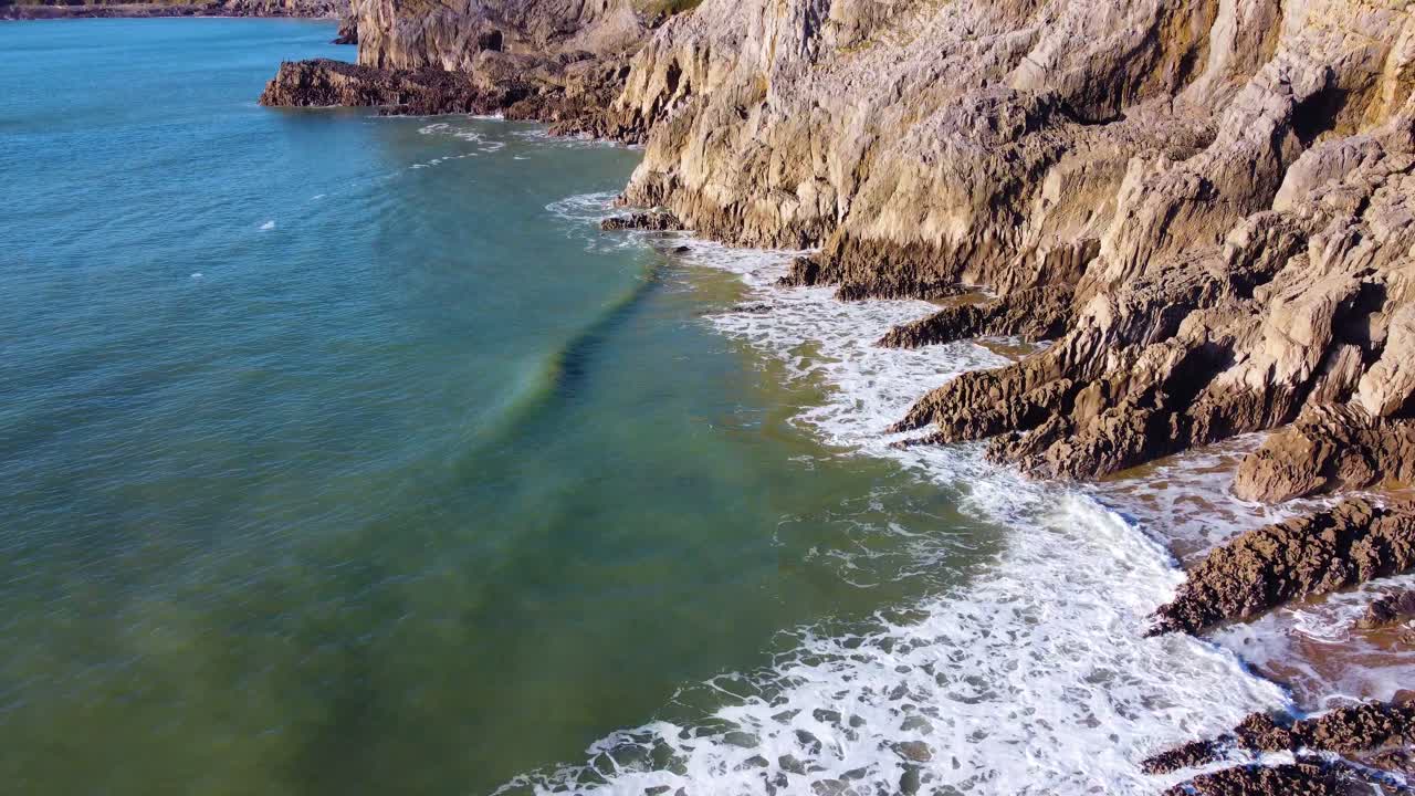 Tilt Up Low Flying Aerial Reveal of Inaccessible Rocky Coastline in Gower, Wales, UK. Rolling Waves Crashing on Rocks Below. Travel Nature Drone Clip