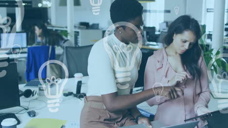 Animation-of-light-bulb-icons-over-diverse-female-coworkers-discussing-reports-on-digital-tablet