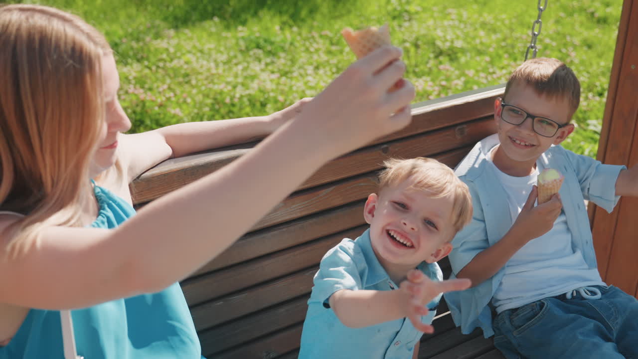 Caucasian family park sharing ice cream, sister savors cone while little brother reaches, older brother enjoys treat on bench, sunlit backdrop, gentle sibling care, relaxed weekend afternoon and warm