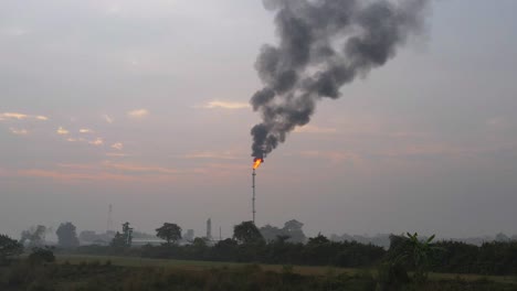 flying across green fields toward tall chimney to reveal a large factory below