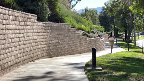 una mujer adulta trotando a lo largo de una acera de la ciudad suburbana en un día de verano en cámara lenta