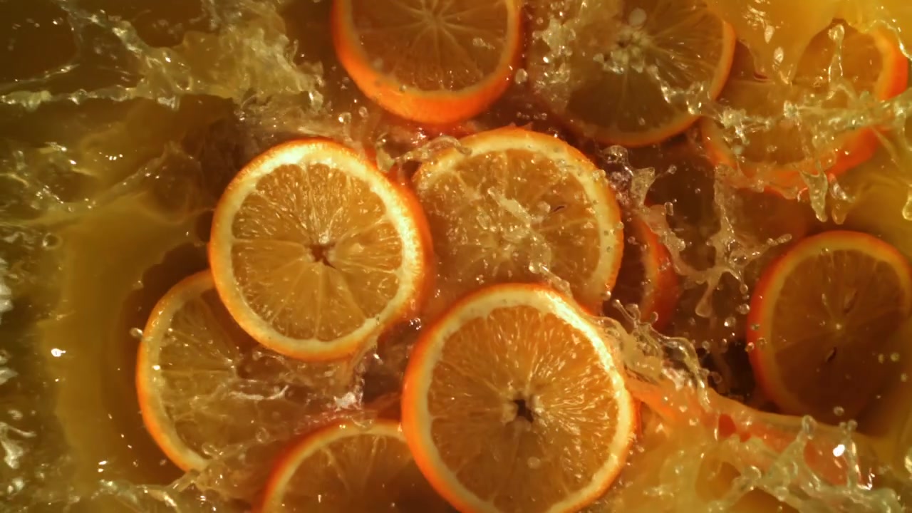 Fette d'arancia che cadono e schizzano nel succo d'arancia fresco al rallentatore