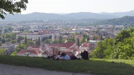 una pareja descansando en el césped con una vista panorámica de ljubljana en eslovenia