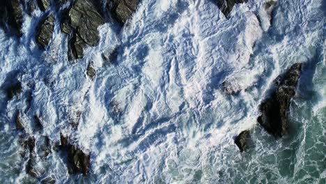 top down view over rocky coastline with ocean waves in slow motion